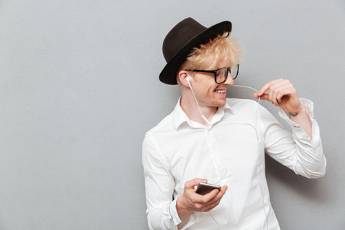 A stylish man wearing a hat and headphones, wondering if wearing hats can cause hair loss.