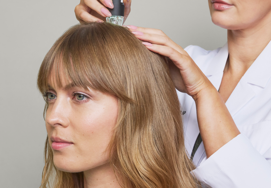A woman receiving a PRP hair treatment on the top of her head, with a healthcare professional applying a specialized device to her scalp.